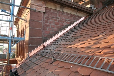 Hier, wo das Dach an den Turm grenzt, waren die Ziegel bisher mit M&ouml;rtel zum Mauerwerk hin abgedichtet. 

Dieser war sehr br&uuml;chig und teilweise bereits abgefallen. Somit konnte Feuchtigkeit in den Dachstuhl darunter eindringen.

Deshalb wurde auch hier eine Kupferverblechung angebracht um den Dachstuhl dauerhaft vor endringender N&auml;sse zu sch&uuml;tzen.