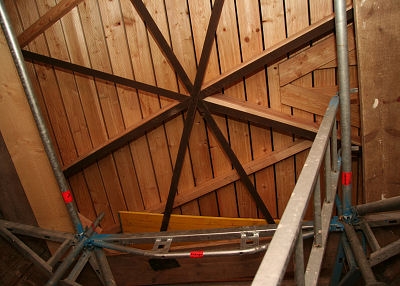 Steigt man im Turminneren auf das Ger&uuml;st &uuml;ber dem Glockenstuhl, so sieht man, die Zimmerleute bereits den neuen Zwischenboden zum Turmhelm eingebaut haben.

Die alten Stahlb&auml;nder werden nun durch dicke Holzbalken verst&auml;rkt.
